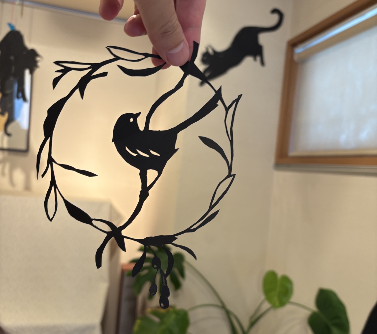 手に持たれた切り絵の小鳥と、壁に映る猫の影